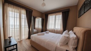 A spacious bedroom with a large bed, a bedside table, a mirror, and a window with curtains. - Servi House (Akçaabat)