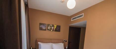 A hotel room with a large bed, a nightstand, a lamp, and a door.