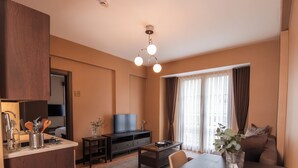 A modern living room with a wooden dining table, a sofa, a TV, and a kitchen area with a countertop and cabinets. - Servi House (Akçaabat)
