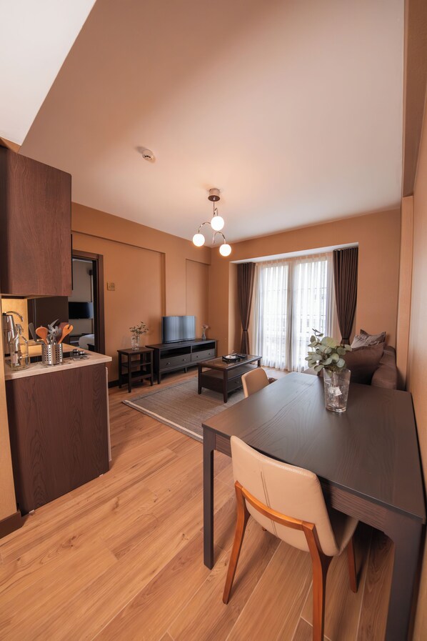 Un salon moderne comprenant une table à manger en bois, un canapé, un téléviseur et un coin cuisine avec un plan de travail et des placards.