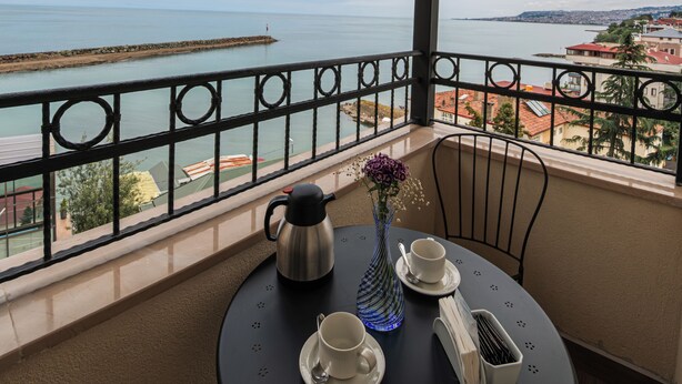 A balcony with a table set for two, overlooking a body of water and a distant cityscape. - Servi House (Akçaabat)
