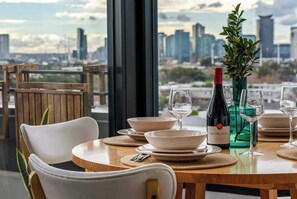 A dining table set with plates, bowls, and wine glasses, with a bottle of Red Hill Estate wine and a green vase with a plant. - City Meets The Sea Melbourne Penthouse (Melbourne)