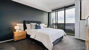 Una camera da letto moderna con un letto grande, pareti scure e vista attraverso una porta scorrevole.