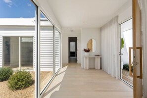 A modern, minimalist hallway with a wooden floor, large sliding glass doors, and a small white console table with a mirror. - The Pavilion in Mount Martha (Melbourne)