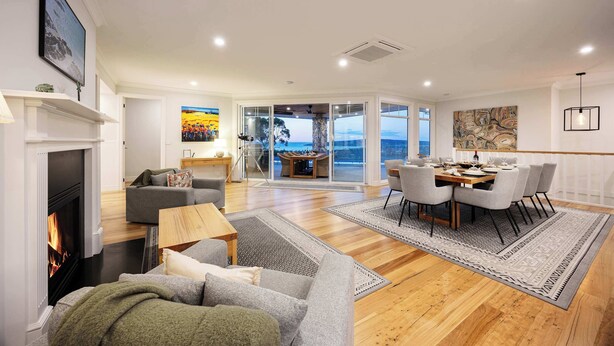 A spacious living area with a fireplace, a dining table with chairs, and a view through glass doors to the outdoors. - Baymere Pool Spa City Views (Melbourne)