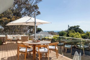 Eine Holzterrasse mit rundem Tisch und Stühlen sowie Gartenmöbeln und einem großen Sonnenschirm.