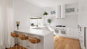 Una cocina moderna con armarios blancos, una isla central con taburetes y vistas al exterior.