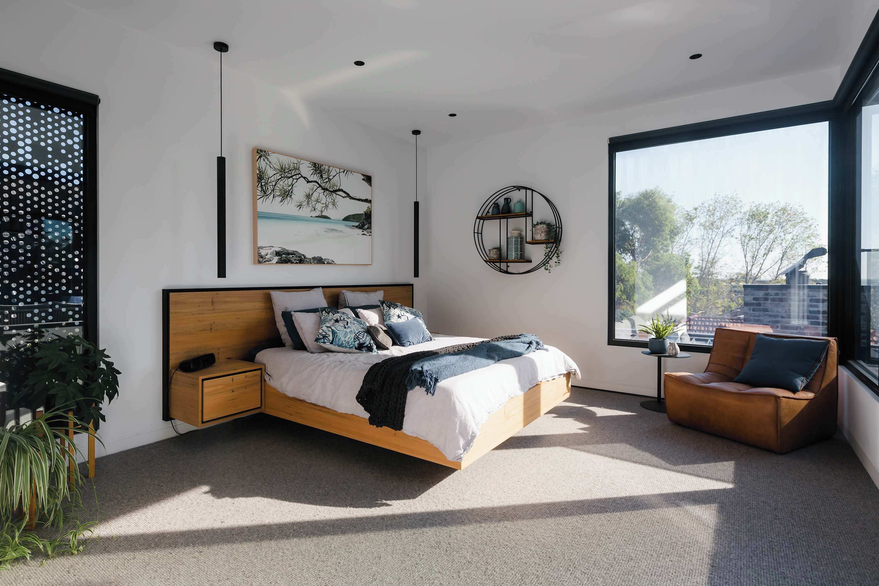 A modern bedroom with a large bed, a side table, a round side table with a plant, a sofa, and a large window with a view of the outside.