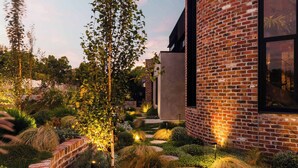 A modern brick building with a large window and a well-maintained garden with various plants and a stone pathway. - Helix in Mornington With 4 Bedrooms and 3 5 Bathrooms (Melbourne)