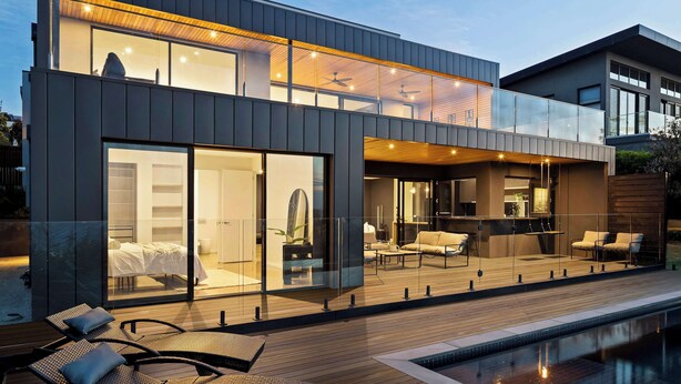 Et moderne hus i to etager med en veranda med glasfacade, en pool og et godt oplyst interiør.