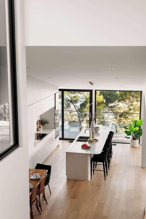 Una cocina moderna con una isla central, ventanas amplias y una zona de comedor con sillas.