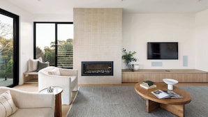 A modern living room with a fireplace, a sofa, a coffee table, and a TV mounted on the wall. - Banksia Luxury Home With Views (Melbourne)