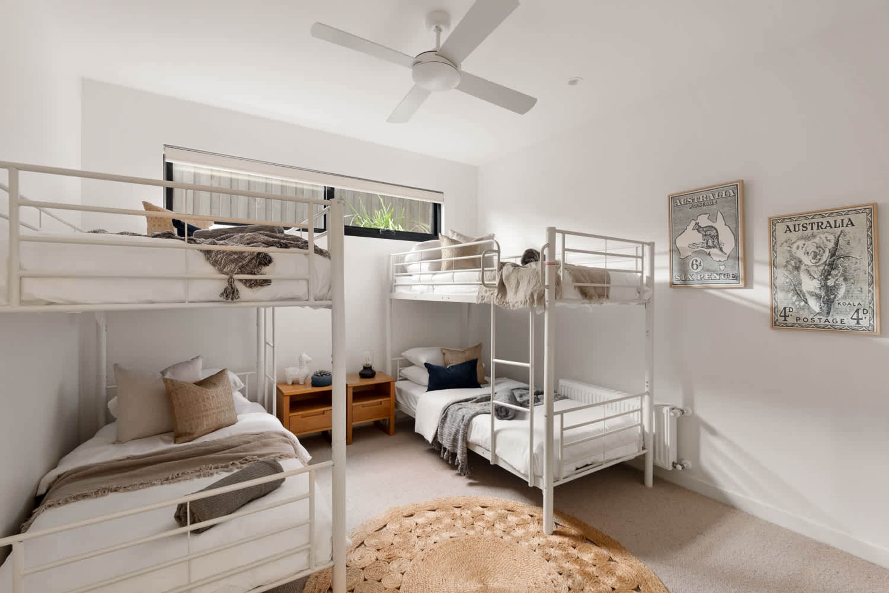 A room with bunk beds, a ceiling fan, a window with a view, and two wall-mounted Australia postage stamps.