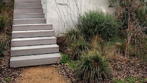 A modern house with a concrete staircase leading to a wooden deck, surrounded by greenery. - Banksia Luxury Home With Views (Melbourne)
