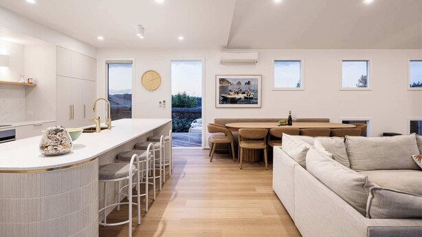 Une cuisine moderne dotée d’un îlot central, de tabourets de bar, d’un coin repas avec une table et des chaises en bois, et d’un espace salon avec un canapé.