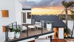 Un balcon moderne avec des meubles d’extérieur, une vue sur le coucher de soleil et un palmier.