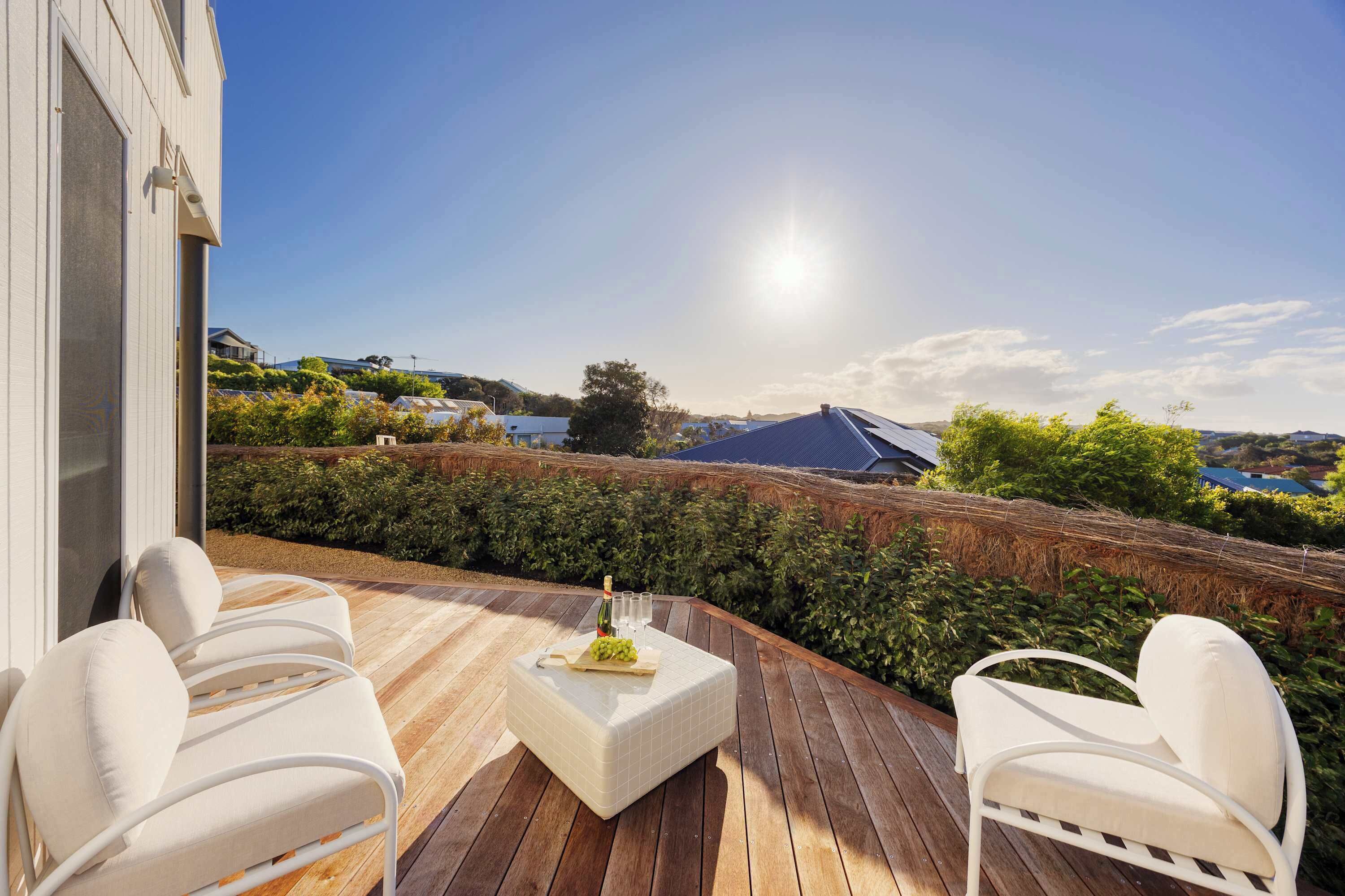 A wooden deck with white cushioned chairs and a table, overlooking a scenic landscape with hills and a body of water.