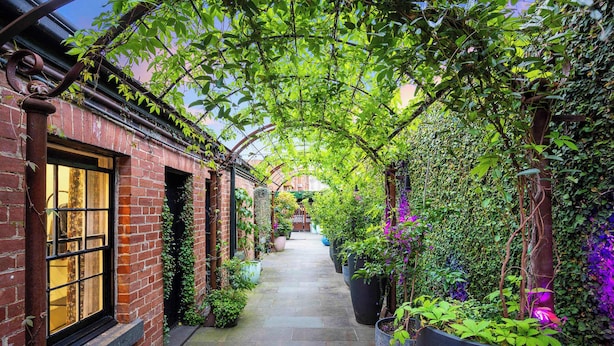 A narrow brick alleyway with a covered walkway, potted plants, and a view of a building in the distance. - The Empress Direct Access Carlton Gardens (Melbourne)
