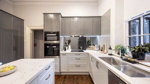 A modern kitchen with grey cabinets, a built-in oven, a stainless steel sink, and a marble countertop. - The Empress Direct Access Carlton Gardens (Melbourne)