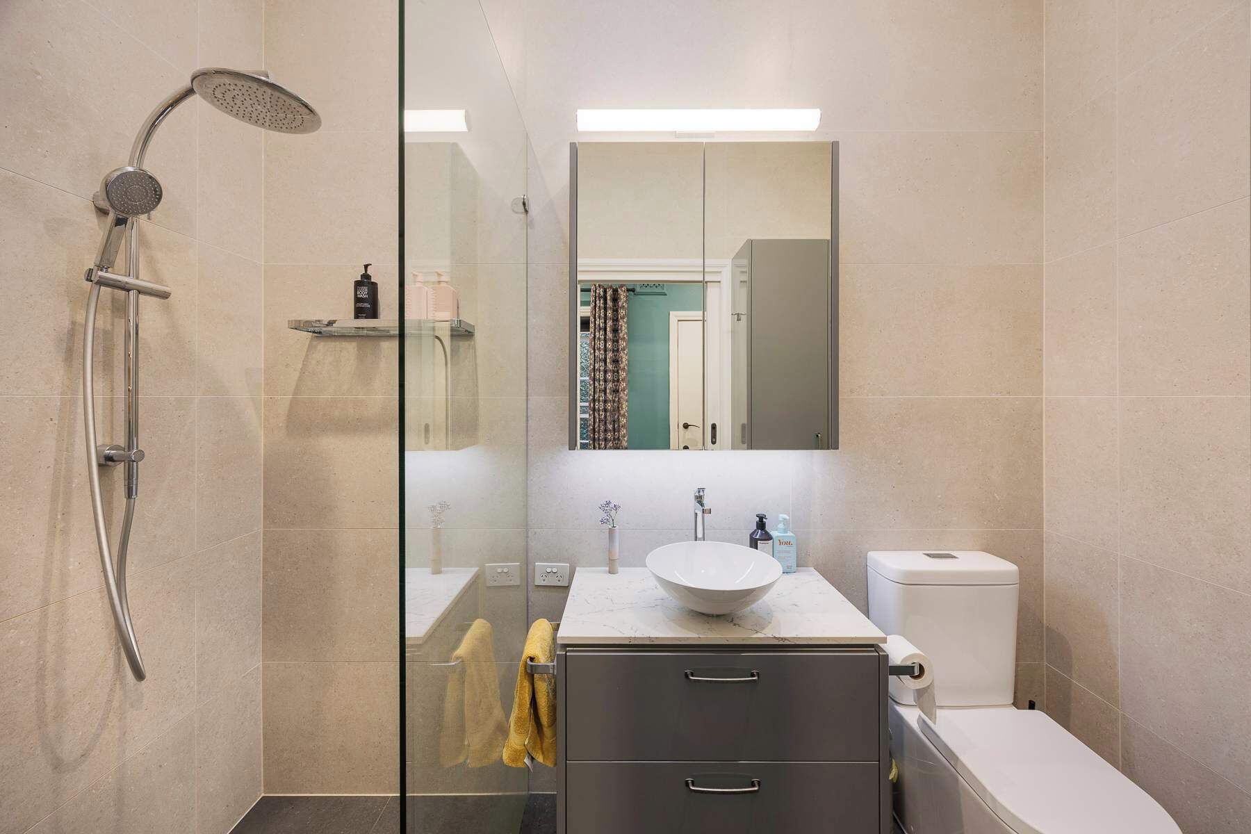 Een moderne badkamer met een douchecabine van glas, een witte wastafel en een toilet.