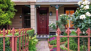 A traditional building with a red door, numbered 62, and a small garden with a variety of plants and flowers. - The Empress Direct Access Carlton Gardens (Melbourne)