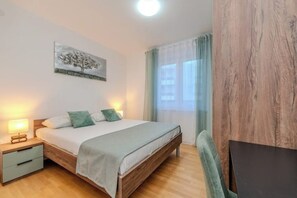 A bedroom with a wooden bed, bedside tables, a nightstand, a painting on the wall, and a window with curtains. - Villa Anita apartments 2 (Novalja)