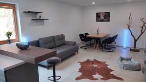 A modern living room with a grey sofa, a wooden coffee table, a dining table with chairs, a cowhide rug, and a small tree in a pot. - Holly-WOOD Allgäu vacation apartment - relaxation with heart in the countryside (Markt Rettenbach)