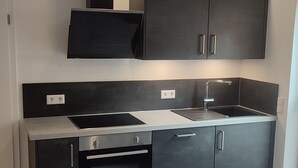 A modern kitchen with dark cabinetry, a built-in oven, and a stainless steel sink. - Holly-WOOD Allgäu vacation apartment - relaxation with heart in the countryside (Markt Rettenbach)
