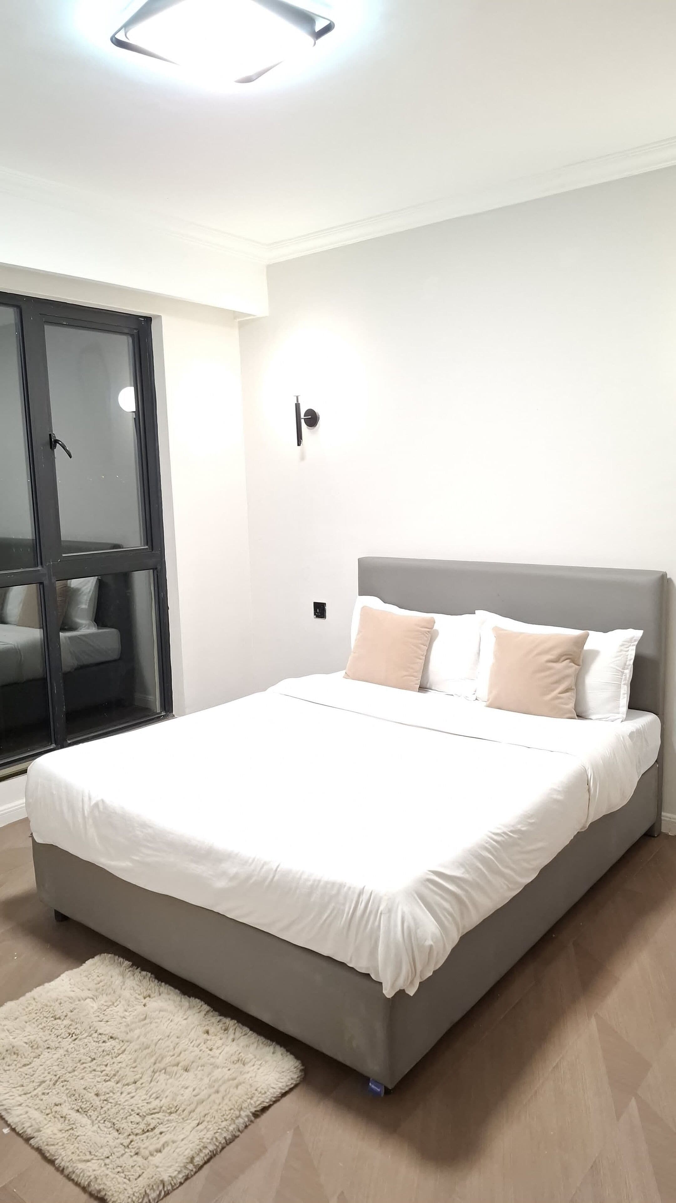 A modern bedroom with a large bed, a sliding glass door, and a small bedside table.