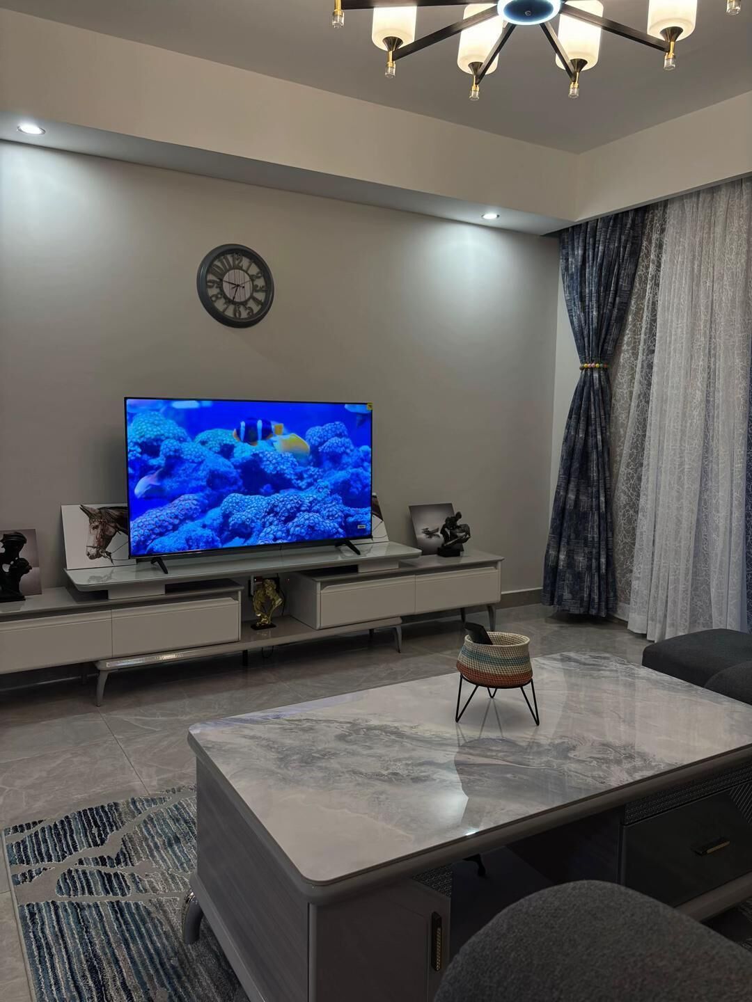 A modern living room with a flat-screen TV, a clock, and a decorative wall piece.