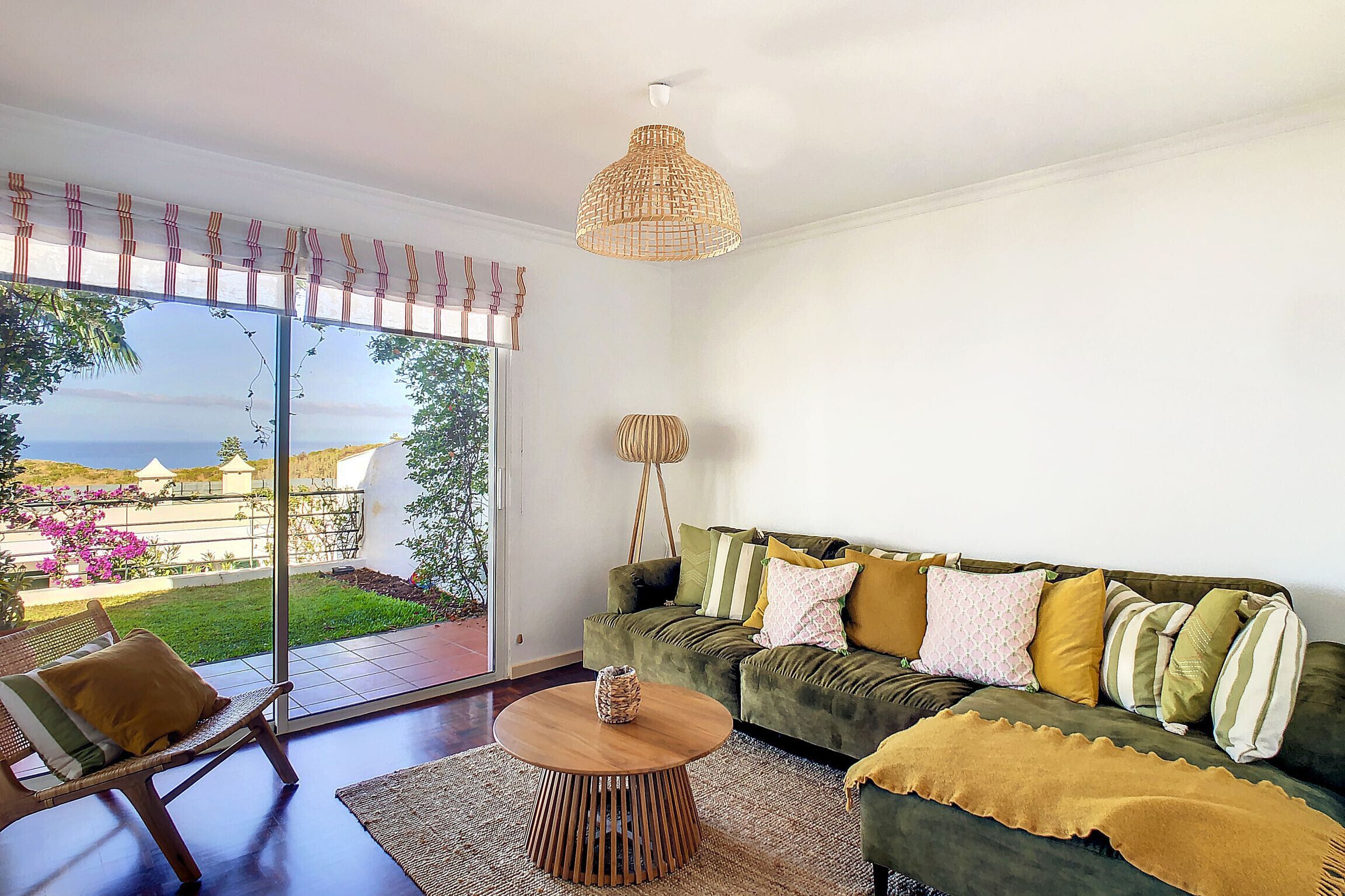 Uma sala de estar espaçosa com um sofá verde, uma mesa de centro de madeira e uma janela grande que oferece vista para um jardim e um edifício.