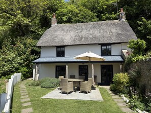 A white building with a thatched roof, a patio with wicker furniture, and a white fence. - Spring Cottage, scenic holiday cottage near the coast (West Lulworth)