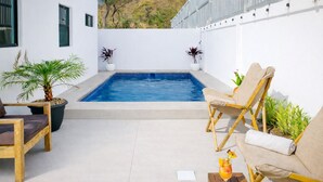 Un espace aménagé au bord de la piscine, comprenant une petite piscine, deux chaises longues, une table en bois et des plantes en pot.