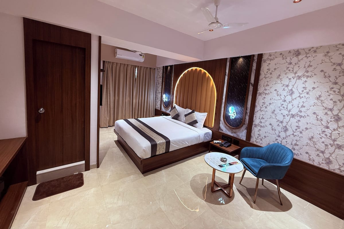 A modern hotel room with a large bed, a small round table, a blue chair, and a ceiling fan.