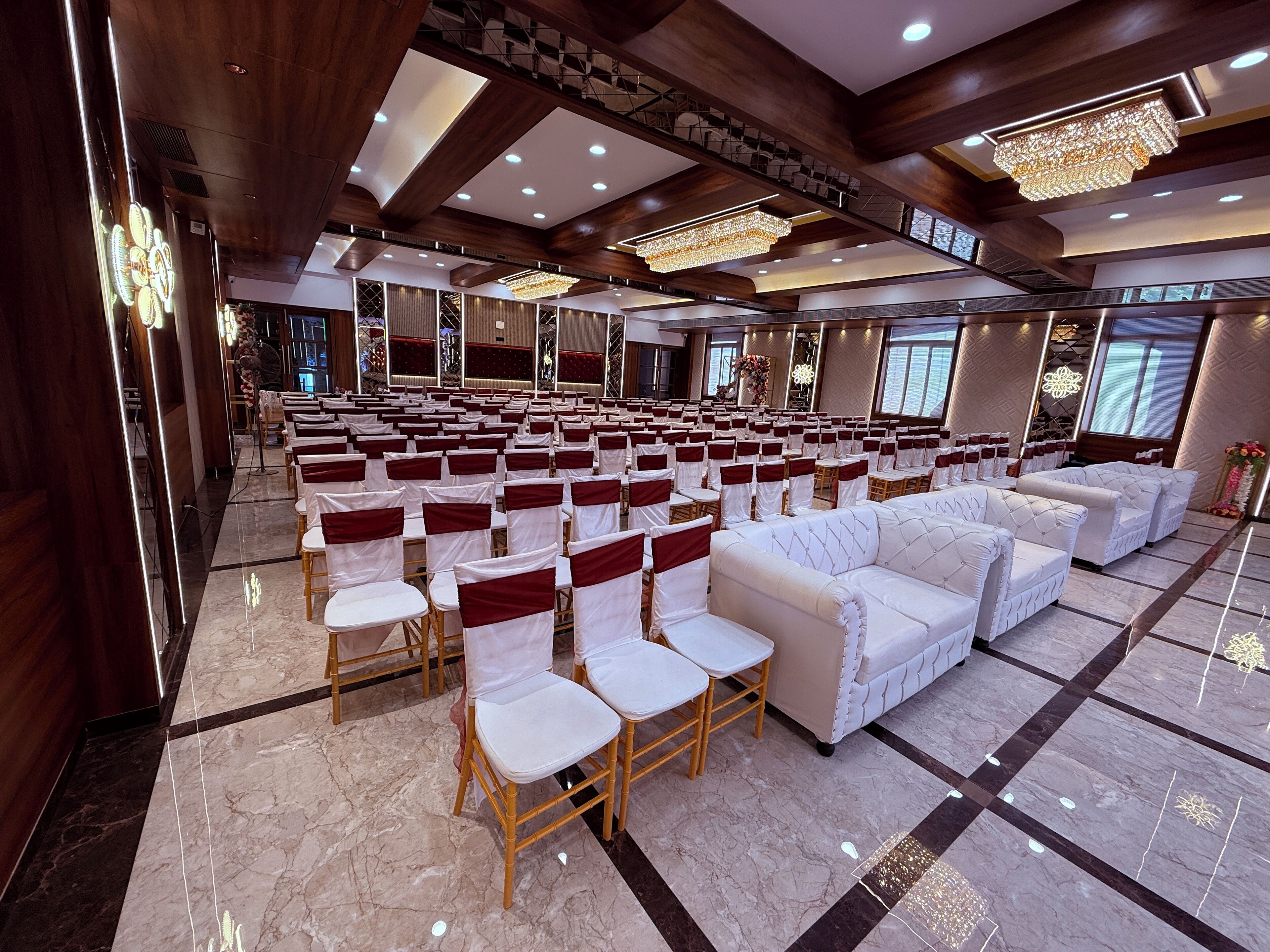 A spacious hall with rows of white chairs and sofas, wooden paneling, and a chandelier.