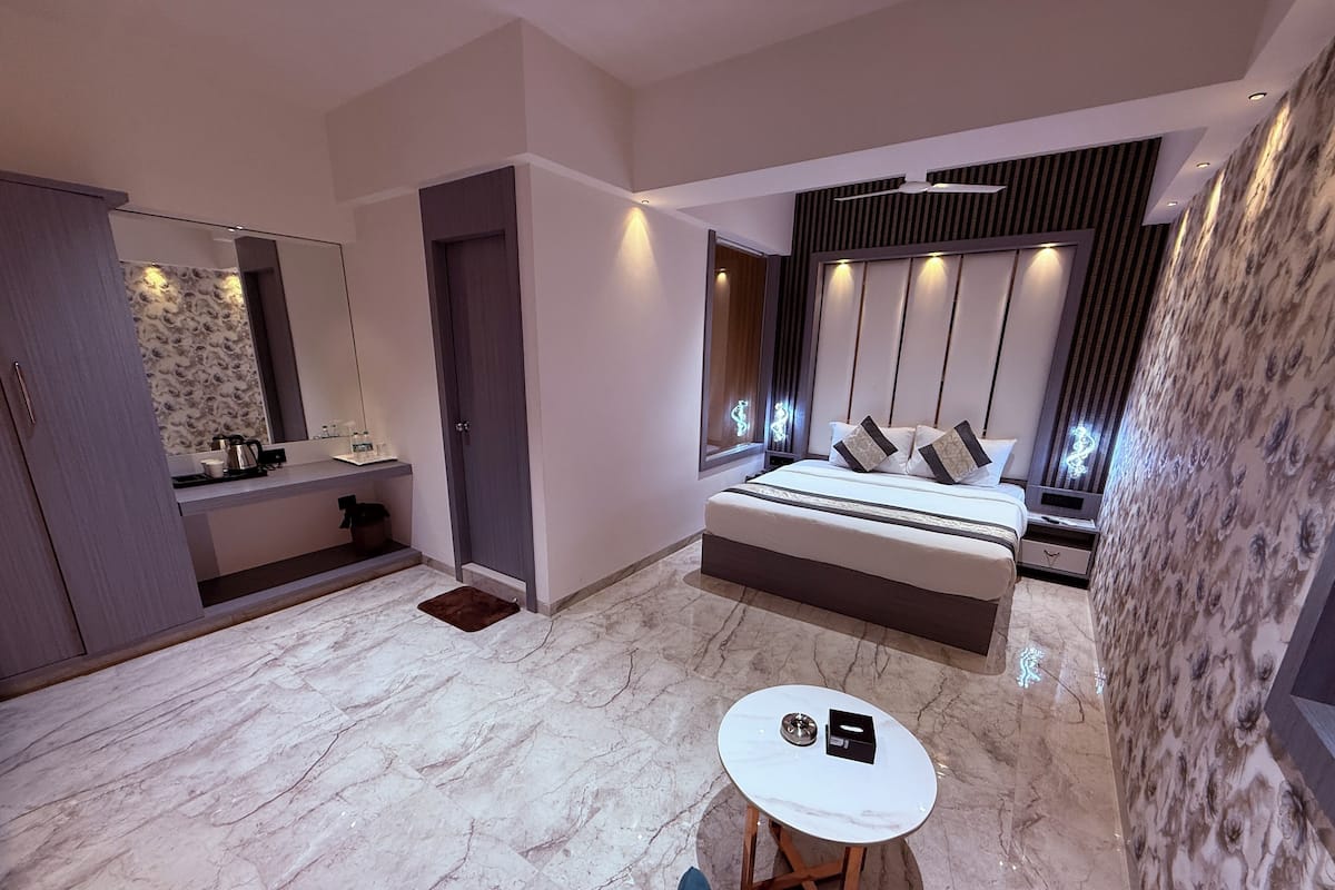 A modern bedroom with a large bed, a bedside table, a small round table, and a bathroom with a mirror and sink.