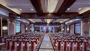 Un salón de banquetes con filas de mesas y sillas, una araña y un escenario con un telón de fondo.