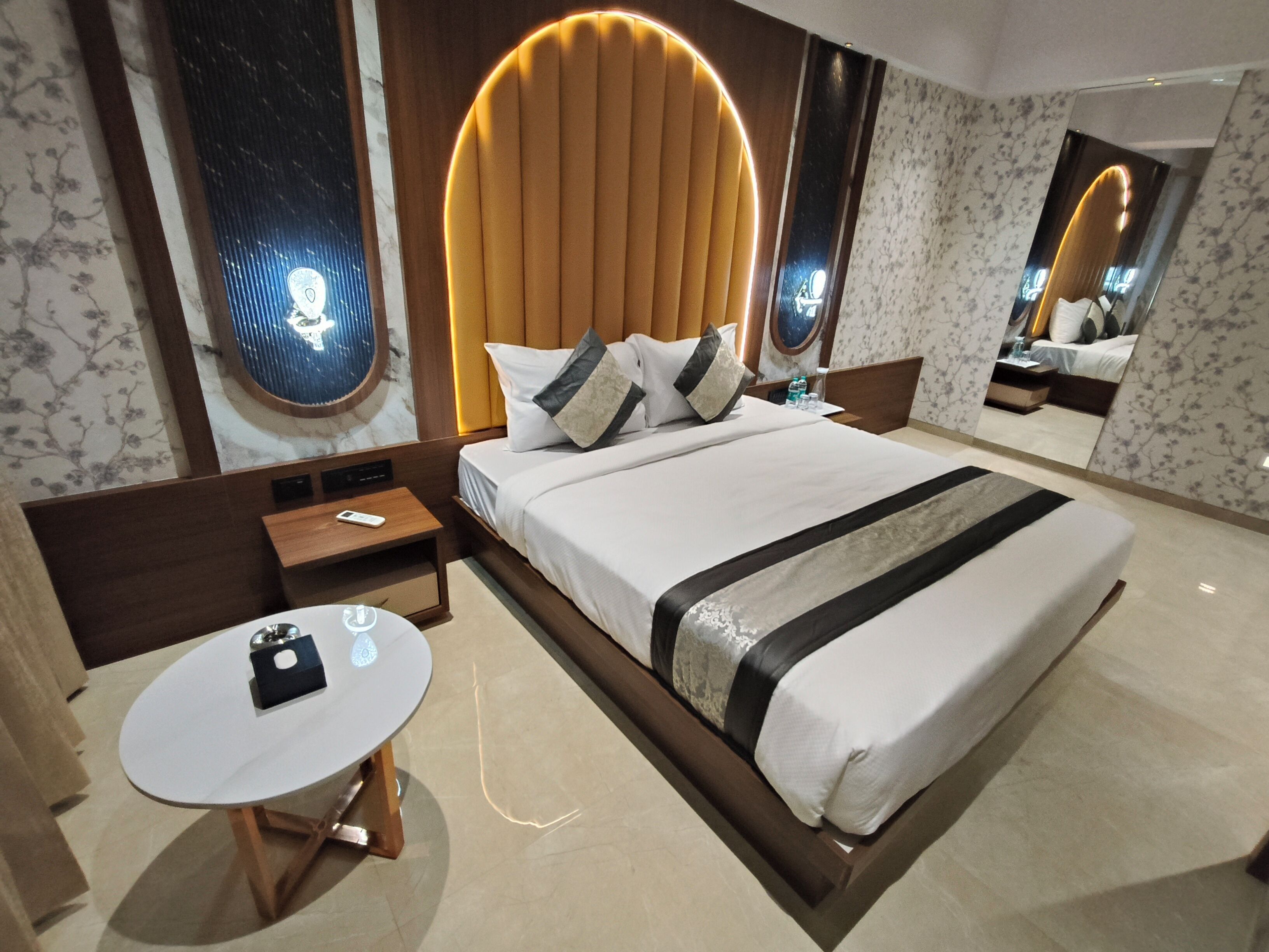 A modern hotel room with a large bed, a round table, and a mirror.