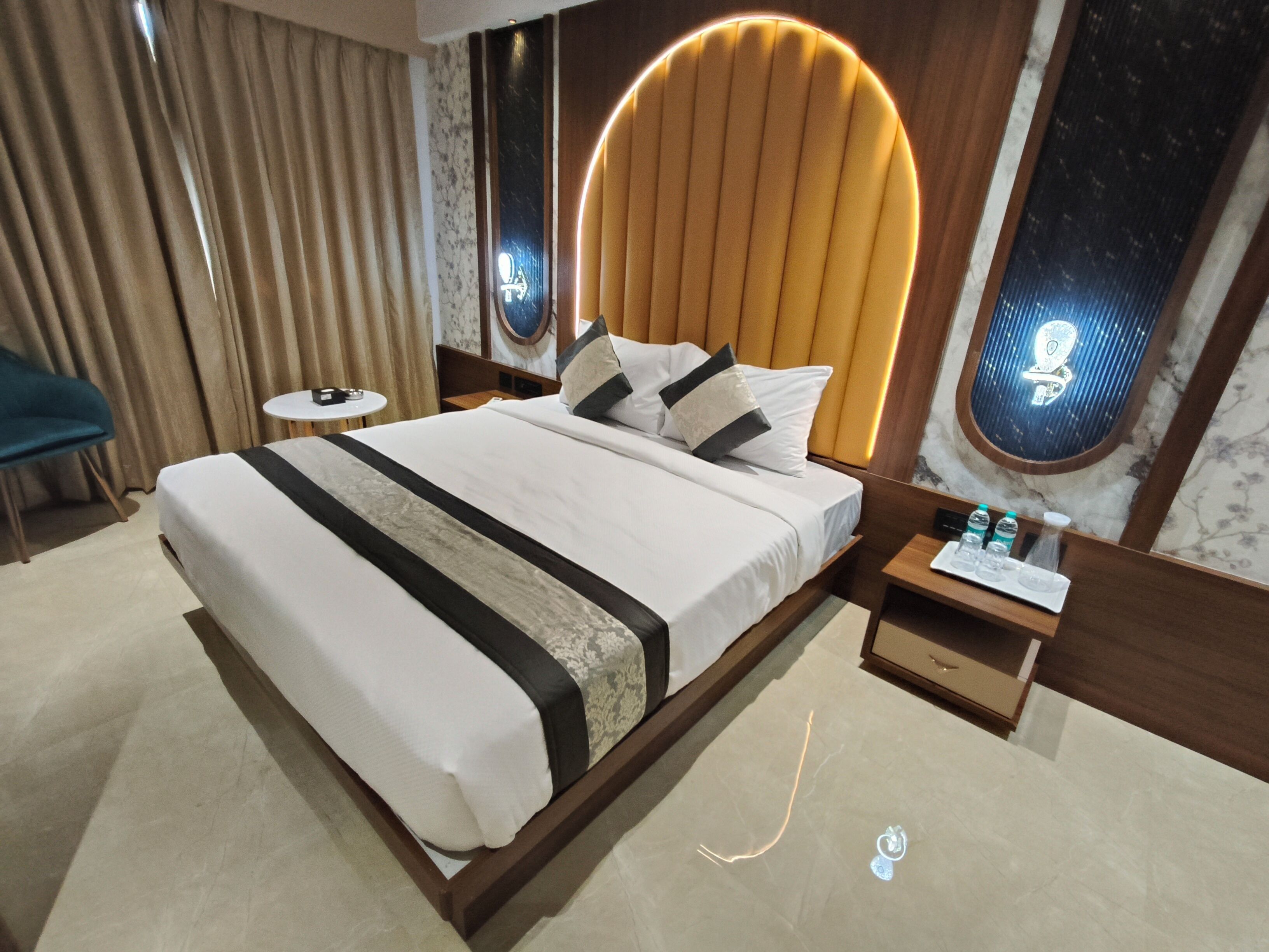 Una habitación de hotel moderna con una cama grande, una mesita de noche con artículos de aseo, un espejo redondo y vistas al cielo nocturno a través de una ventana.