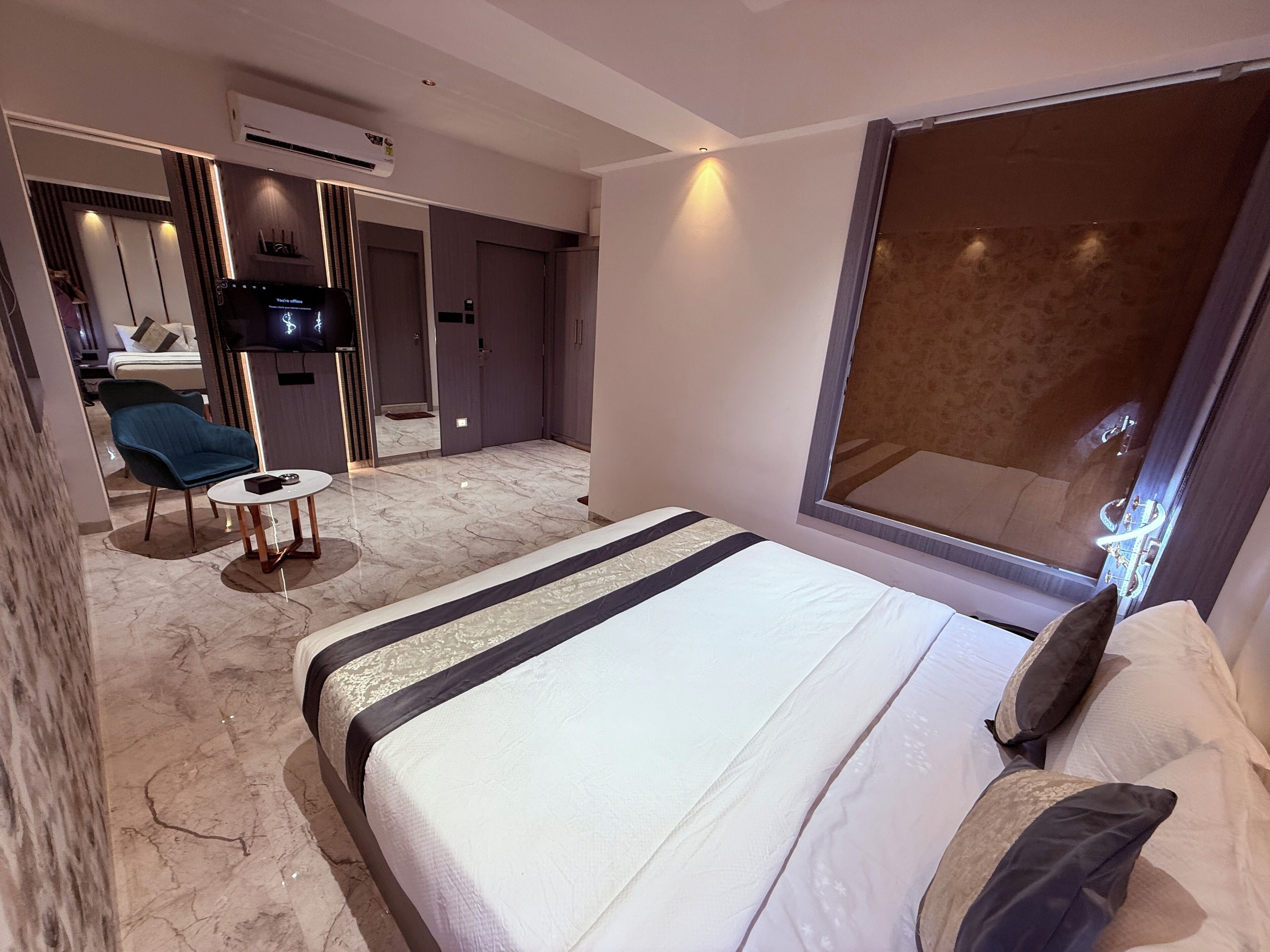 Una habitación de hotel moderna con una cama grande, una pequeña mesa redonda, una silla, un televisor y un ventanal amplio.