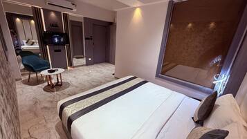 Una habitación de hotel moderna con una cama grande, una pequeña mesa redonda, una silla, un televisor y un ventanal amplio.