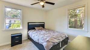 Een slaapkamer met een bed, nachtkastje, bureau en plafondventilator.
