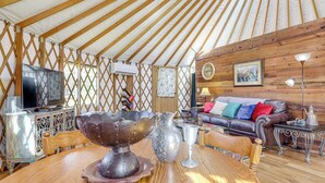 Ein traditionelles Jurten-Interieur mit Holztisch, einer Couch und einem Fernseher.
