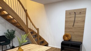 A modern interior with a wooden staircase, a dining table with cushioned benches, a potted plant, and a wall-mounted wooden board. - Be Grand Apartments Rust (Rust)