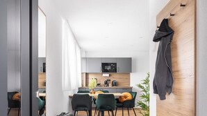 A modern, minimalist hotel room with a wooden floor, a dark grey wardrobe, a bench, and a dining area with green chairs and a wooden table. - Be Grand Apartments Rust (Rust)