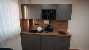 A compact kitchenette with a microwave, coffee maker, and a small countertop. - Be Grand Apartments Rust (Rust)