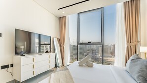 A modern hotel room with a large bed, a flat-screen TV, a white dresser, and a city view through large windows. - Mins from City Walk, Downtown Dubai and Jumeirah Beach, Easy Access to Metro Stations (Dubai)