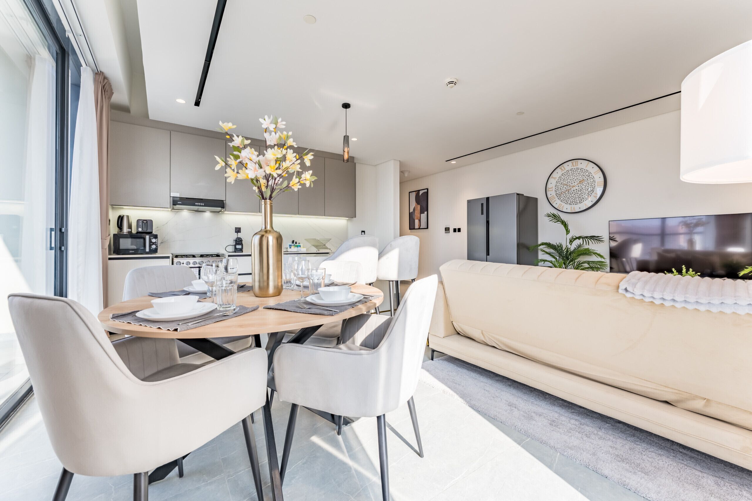 Una sala de estar moderna con sofá, una mesa de comedor con sillas, una zona de cocina y un televisor grande.