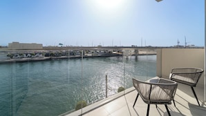 A balcony with two wicker chairs, a glass railing, and a view of a canal with boats and a bridge in the distance. - 2BR M Canal Front B3 Waterfront Views (Dubai)