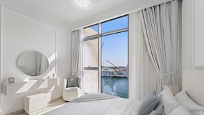 A modern bedroom with a large bed, a vanity with a mirror, and a view of the water. - 2BR M Canal Front B3 Waterfront Views (Dubai)